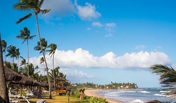 Praia paradisíaca com coqueiros, areia branca e mar azul sob céu parcialmente nublado, ideal para aproveitar o sol e o mar em um destino tropical. Férias na Montanha ou na Praia.