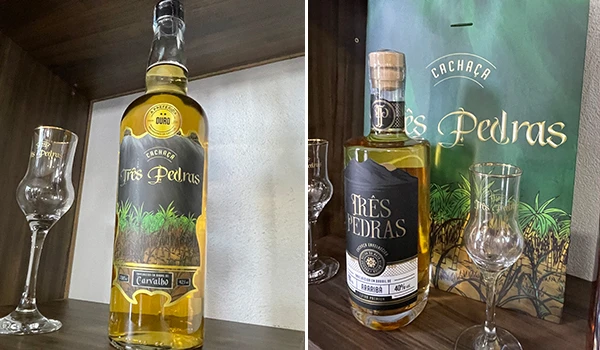 Imagem de uma garrafa de cachaça Três Pedras em destaque, acompanhada por dois copos de vidro. Rotas Gastronômicas do interior de SP.