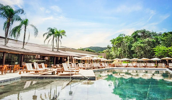 Piscina ao ar livre em um resort com espreguiçadeiras, guarda-sóis, palmeiras e área de lazer com vista para a natureza, céu azul e ambiente relaxante. Um lugares para comemorar Bodas de Prata no Brasil.