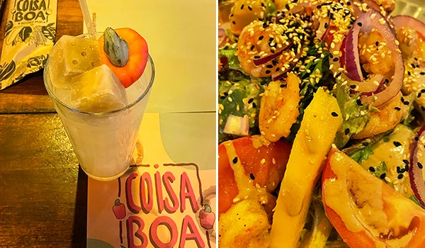 Um drink com caju e pedaços de frutas, servido em copo alto com uma colher de metal, ao lado de uma deliciosa salada de frango com vegetais e sementes, ideal para refeições leves. Rotas Gastronômicas do interior de SP.