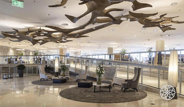 Lobby de hotel moderna com cadeiras confortáveis, várias plantas, iluminação suave e objetos decorativos elegantes, criando um ambiente acolhedor e sofisticado.