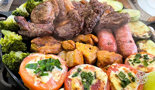 Prato de carne com legumes, tomate recheado com queijo, brócolis e outro tipo de carne grelhada, ideal para refeições tradicionais.
