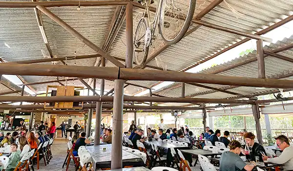 Foto de um restaurante movimentada com muitas pessoas sentadas em mesas, ambiente casual com estrutura de ferro e teto metálico, decorado de forma moderna e informal. Rotas Gastronômicas do interior de SP.