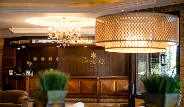 Imagem que mostra um elegante ambiente de hotel ou restaurante com iluminação sofisticada, decoração moderna e recepção com detalhes decorativos em madeira, perfeito para uma experiência de hospedagem ou um evento especial.