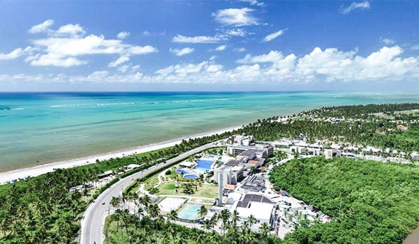 Vista aérea de uma praia paradisíaca com mar azul, areias brancas e vegetação exuberante ao fundo, ideal para turismo e lazer. Um lugares para comemorar Bodas de Prata no Brasil.
