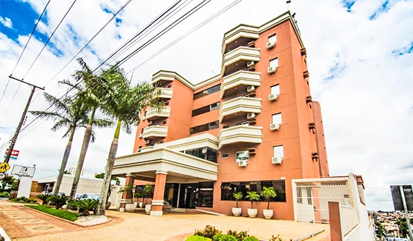Imagem de um hotel com fachada rosa e áreas de lazer na cidade, sob céu parcialmente nublado, ideal para hospedagem em Marília.
