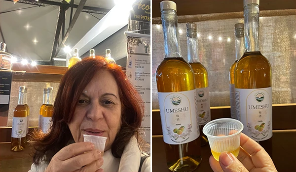 Deusa Rodrigues degustando o licor Umeshu com garrafas ao fundo e um copo com amostra. Produto de qualidade em destaque.