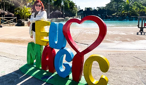 Deusa Rodrigues ao lado de grande letreiro colorido que forma a palavra 'LOVE', em ambiente externo com piscina e natureza ao fundo. Vila Viking e o “Quarto do Rei”.