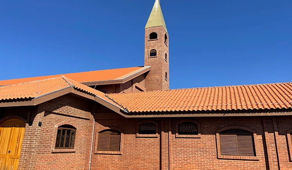 Imagem da fachada de um Mosteiro de tijolos com telhado de telhas alaranjadas e torre de sino alta sob céu claro, cenário típico de arquitetura religiosa brasileira, sobre o que fazer em Marília.