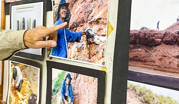 Pessoa apontando para fotos de viagens de aventura em uma parede de exibição, destacando experiências ao ar livre e exploração na natureza.