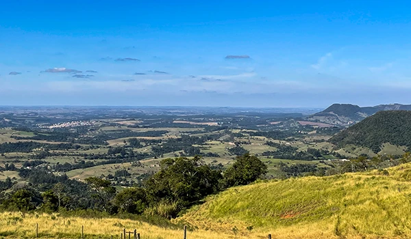 Paisagem de campos verdes e morros ao longe sob céu azul com nuvens suaves, capturada em uma área rural tranquila no Polo Cuesta.