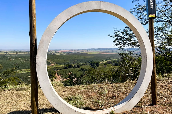 Paisagem vista através de um grande círculo de concreto em um ponto turístico, com vista para o horizonte de áreas verdes, campos e céu azul limpo, ideal para fotos e apreciação da natureza.