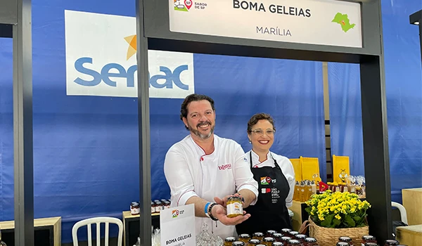 Mesa da Boma Geleias, com destaque em Marília oferecendo geleias artesanais em um estande colorido e atraente.