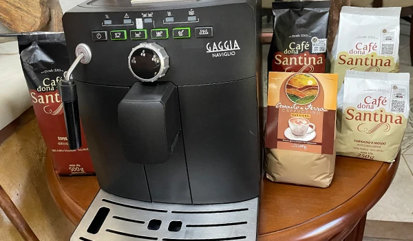 Máquina de café Gaggia Naviglio ao lado de pacotes de café Dona Santina na mesa de madeira. Perfeita para preparar café espresso em casa.