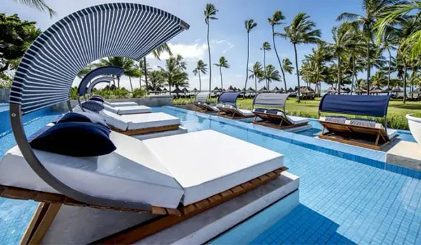 Piscina de resort com espreguiçadeiras confortáveis, espelho d'água, guarda-sol moderno e vista para um cenário tropical com palmeiras ao fundo, perfeito para relaxar e aproveitar o clima quente.
