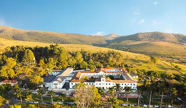Vista panorâmica do Hotel Vila Galé Ouro Preto, rfdeado por natureza, com prédios brancos e árvores verdes sob um céu azul. Um lugares para comemorar Bodas de Prata no Brasil.