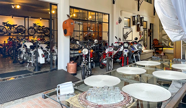 Interior da Garage Zapata com mesas e cadeiras na frente, e ao fundo, uma loja com diversas motos. Rotas Gastronômicas do interior de SP.