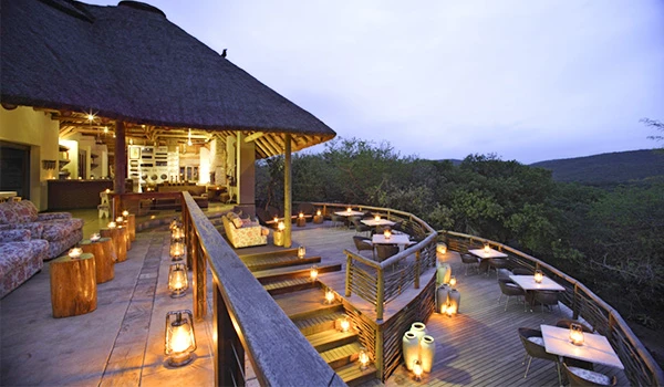 Imagem de um restaurante ao ar livre em uma varanda com decoração aconchegante, iluminação suave, mesas e cadeiras, vista para uma vegetação exuberante, perfeito para experiências gastronômicas ao ar livre.