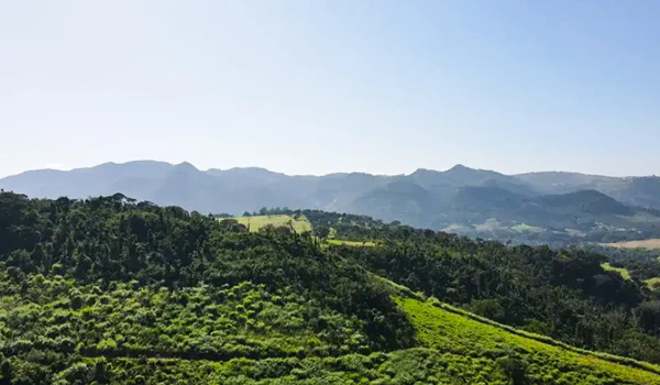 Paisagem de montanhas verdes e colinas sob céu claro, destacando a beleza natural de um cenário montanhoso e rural no Brasil.