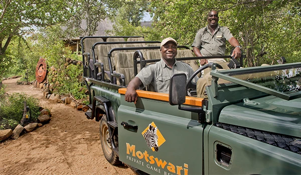 Dois gestores do Motswari Private Game Reserve em safári na África do Sul, aproveitando o turismo de aventura e a experiência de vida selvagem, com árvores verdes ao fundo.