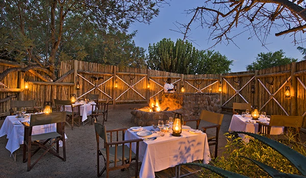 Dicas do Boma jantar savanas África, ao ar livre em restaurante com mesas, cadeiras, iluminação ambiente, fogo artificial e decoração aconchegante durante a noite ao ar livre.