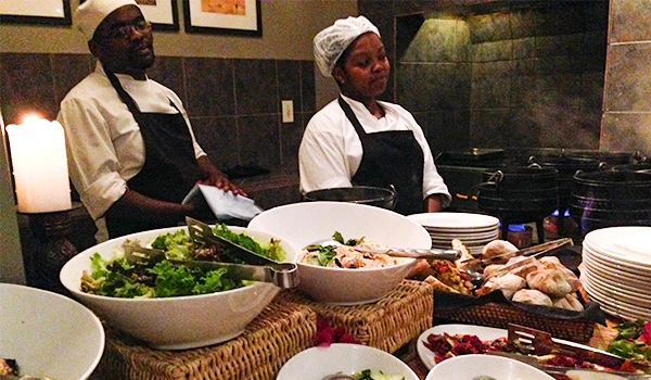 Cozinheiros afro-americanos preparando comida em uma cozinha profissional, com pratos de salada e outros alimentos sobre a bancada. Dicas do Boma jantar savanas África.