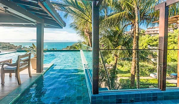 Piscina de borda infinita com vista para o mar, rodeada de palmeiras e uma área de lazer ao ar livre em um ambiente tropical e relaxante. Armação dos Búzios hotéis Lua de Mel.