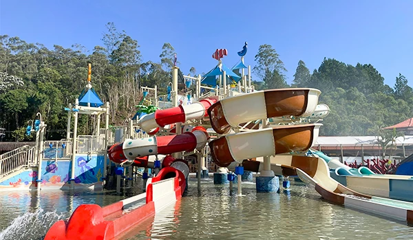 Parque aquático com escorregadores coloridos e áreas de lazer na água, ideal para diversão em família e dias quentes de verão, com árvores ao fundo.