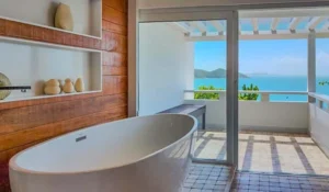Banheira de hidromassagem em varanda com vista para o mar e ilha, ambiente de spa confortável e relaxante.