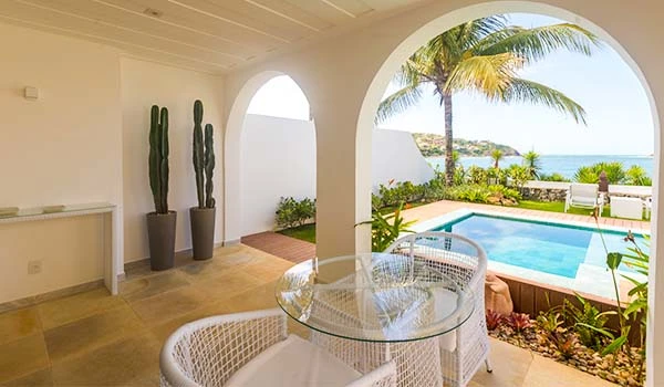 Imagem de uma varanda com vista para uma piscina ao ar livre, com plantas tropicais e vista para o mar. Armação dos Búzios hotéis para Lua de Mel.