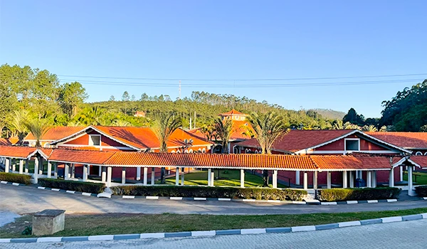 Imagem de uma área residencial com casas de telhado vermelho e jardins bem cuidados, cercada por árvores e com céu claro ao fundo, transmitindo tranquilidade e características de uma vizinhança organizada.