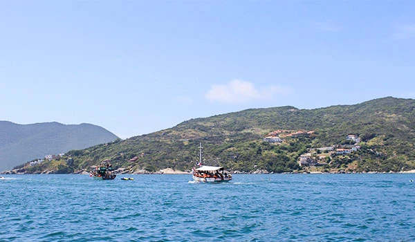 Lindíssima vista de um mar calmo com embarcações navegando, cercado por montanhas verdes sob céu azul claro, ideal para atividades de lazer e turismo.