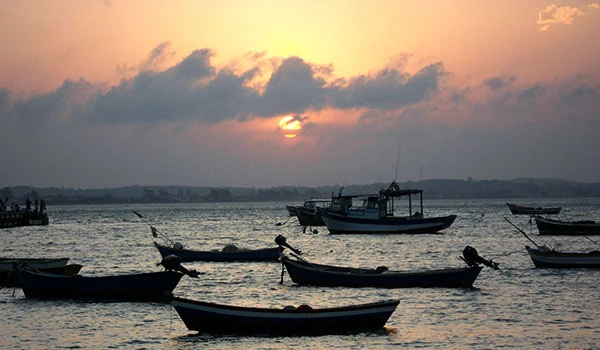 Cenário de pôr do sol com barcos na água e céu com nuvens ao entardecer, refletindo tranquilidade e beleza natural.