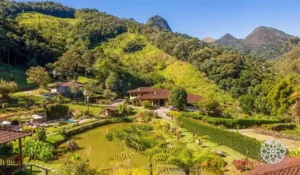 Paisagem exuberante com montanhas verdes, lago e casas em uma área de natureza no Brasil, ideal para turismo ecológico e descanso em meio à natureza.