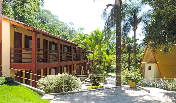 Imagem de uma casa de fazenda com varanda de madeira rodeada por árvores e plantas verdes, criando um ambiente tranquilo e natural. Hotéis para Lua de Mel no estado do Rio de Janeiro.