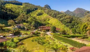 Paisagem de montanhas verdes, com casas, jardim e lago, perfeito para quem busca tranquilidade e contato com a natureza na Serra do Mar.