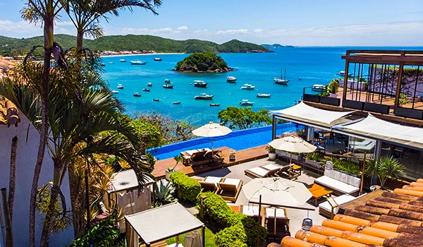Vista deslumbrante com águas azuis cristalinas, muitas embarcações e um resort de luxo com piscina e espaço de lazer ao ar livre. Armação dos Búzios hotéis para Lua de Mel.