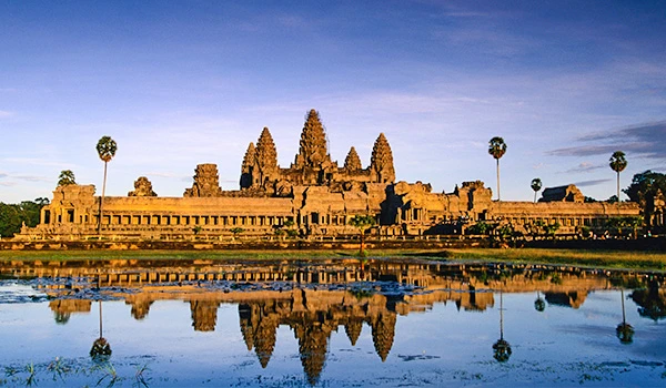 Imagem do Templo de Angkor Wat, um dos maiores monumentos históricos do Camboja, refletido em um lago próximo, sob céu azul claro na Ásia.