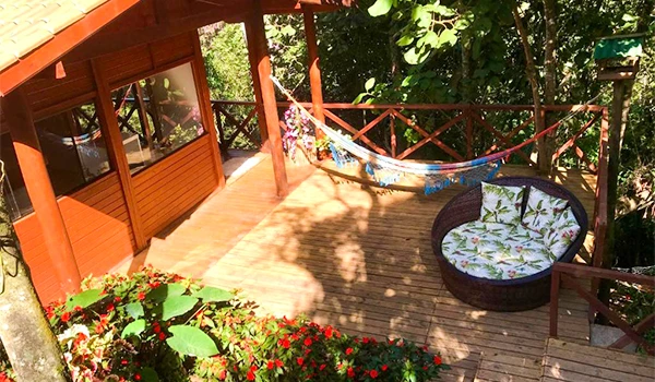 Varanda de madeira com rede, árvore e plantas ao redor, ambiente tranquilo para relaxar ao ar livre em um espaço residencial. Chalés em São Francisco Xavier.