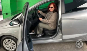 Deusa Rodrigues sentada no carro eletrico, sorrindo enquanto segura o volante na cidade.
