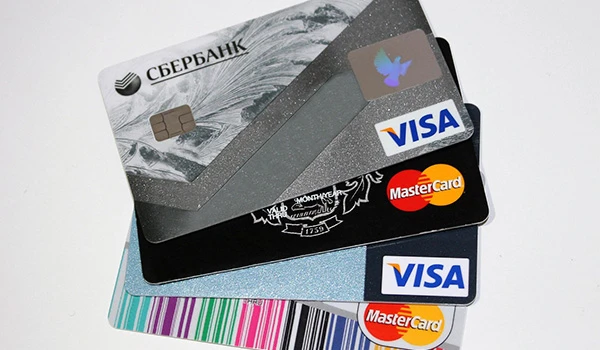 Imagem de cartões de crédito de diferentes bancos e marcas, incluindo Visa e Mastercard, sobre uma mesa branca, destacando opções de pagamento.
