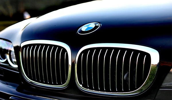 Imagem do capô de um BMW com destaque para sua grade frontal, refletindo o ambiente ao redor e ressaltando o design elegante e moderno do carro.