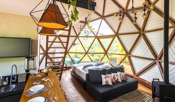 Interior de uma casa com design de geodésico, com parede de janelas panorâmicas, móveis modernos e decoração com plantas, ideal para ambientes aconchegantes e sustentáveis.