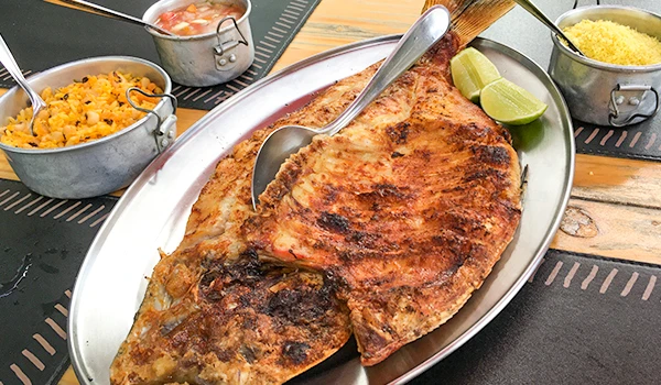 Peixe grelhado servido com limões, acompanhamentos de arroz de açafrão e farofa, ideal para uma refeição de frutos do mar deliciosa.