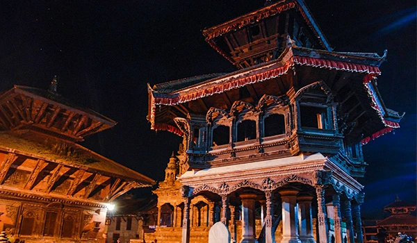 Imagem de um monumento tradicional com detalhes arquitetônicos elaborados, iluminado à noite e com um céu estrelado no fundo.