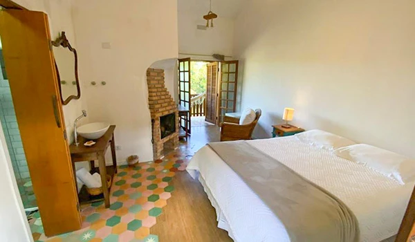 Quarto aconchegante com cama king size, varanda com vista para a natureza, decoração rústica, iluminação suave e espaço confortável para descanso.