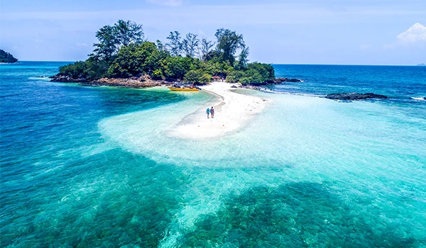 Praia paradisíaca com areia branca e águas cristalinas, cercada por vegetação tropical, ideal para turismo e lazer em ilha tropical