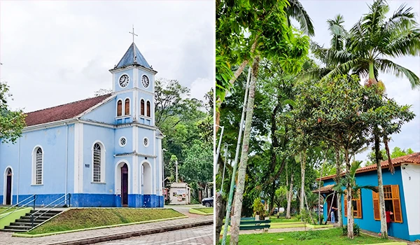 Imagem de uma igreja azul ao lado de uma casa cercada por árvores verdes, incluindo palmeiras, em um cenário tropical ensolarado. Chalés em São Francisco Xavier.