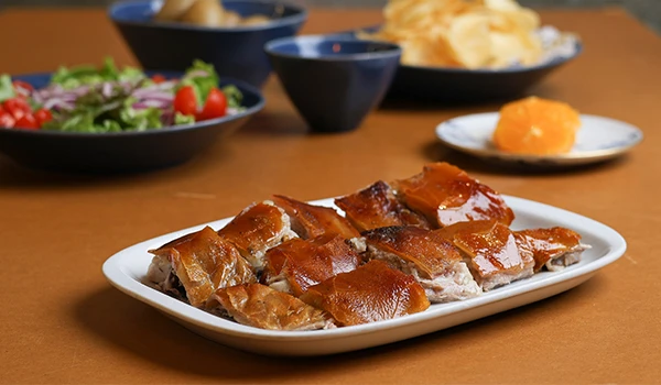 Prato de carne de porto assada com salada, batatas e molho em uma mesa de jantar. Comida deliciosa e bem apresentada, uma das atrações de Coimbra.