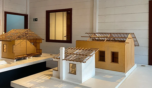 Maquete de casas de arquitetura em uma sala, mostrando detalhes de modelos de construções em madeira com diversos estilos de telhados e estruturas.